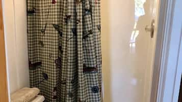 Een badkamer met toilet, een douche met glazen deur en een gordijn met patroon.