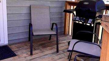 A covered porch with a grill, two chairs, and a wooden deck.
