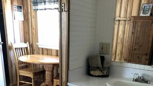 Un interior de madera con una mesa de comedor, sillas, un lavamanos blanco y una alfombra estampada.