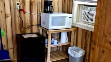Een compacte kitchenette met een magnetron, koffiezetapparaat en een kleine prullenbak.