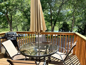 Eine Terrasse mit Glastisch, Stühlen, Grill und Sonnenschirm.