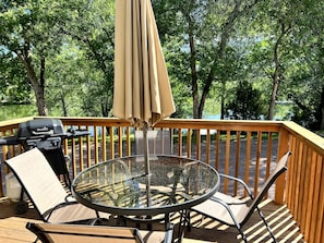 A deck with a glass table, chairs, a grill, and an umbrella.