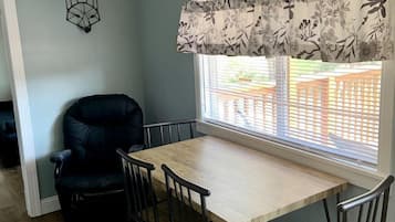 En matplats med ett träbord och stolar, en svart stol, en blommig gardinkappa och en geometrisk väggdekoration.