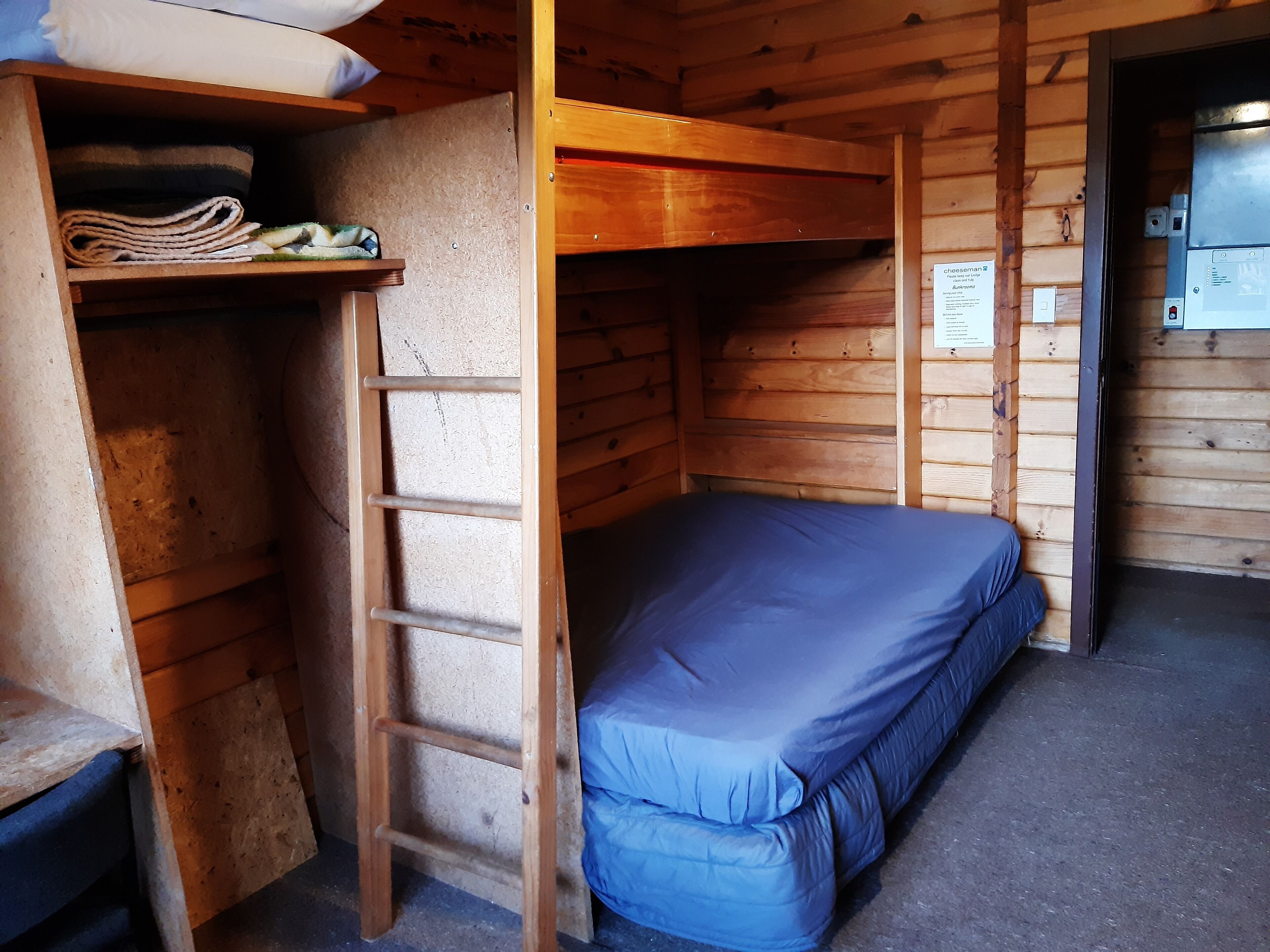 Une petite pièce, de taille modeste, avec un lit superposé, une échelle et une étagère où sont pliées des couvertures.