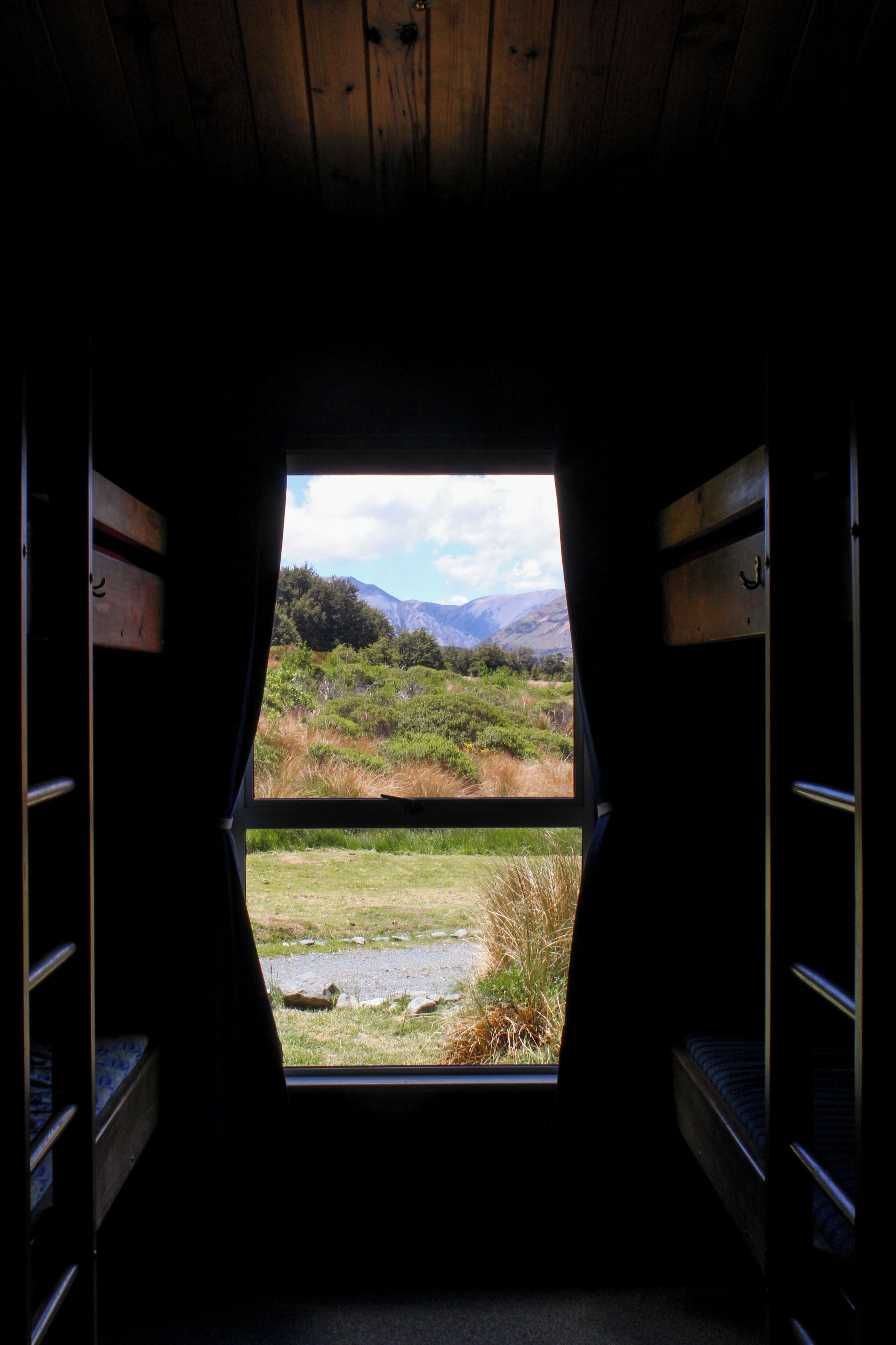 A narrow, dimly lit interior with a large window revealing a grassy landscape and mountains.
