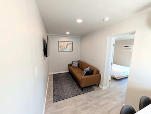 A modern, well-lit room with a brown sofa, a patterned rug, and a bed in the background.