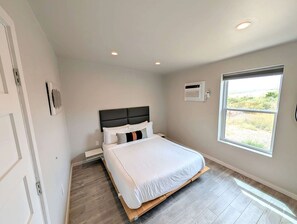 A bedroom with a bed, a nightstand, a window with a view, and a ceiling light.