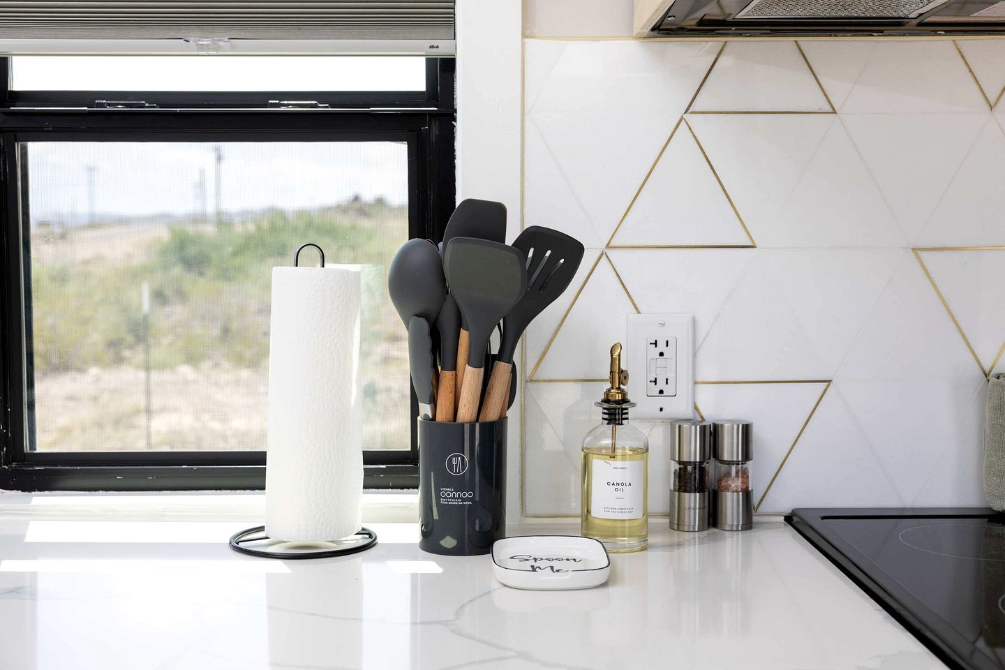 Una encimera de cocina con un rollo de toallas de papel, un recipiente para utensilios con cucharas de madera, una botella de aceite y una especiero.