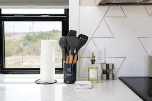 A kitchen counter with a roll of paper towels, a utensil holder with wooden spoons, a bottle of oil, and a spice rack.