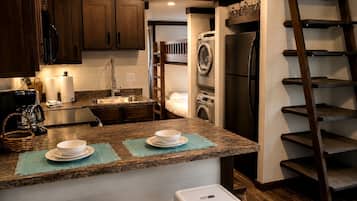 A kitchen with a built-in washer and dryer, a coffee maker, and a wooden ladder.