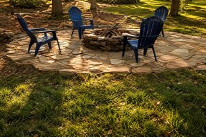 A stone fire pit surrounded by four Adirondack chairs in a garden setting. - Glorious Cabin with Stunning Sights in Monteagle, Tennessee (Monteagle)