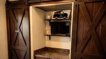 Een kamer met een schuifdeur in landhuisstijl, een televisie op een plank en een klein tafeltje met lades.