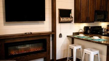 Una cocina moderna con televisor de pantalla plana, chimenea, armarios de madera, microondas y cafetera.