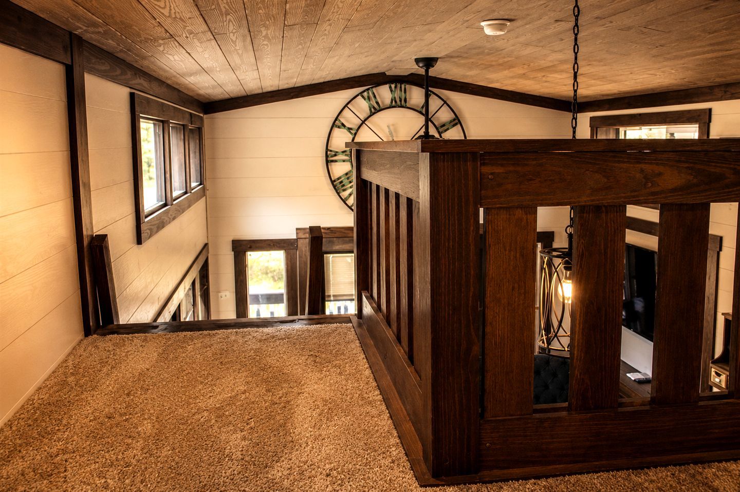 A wooden staircase with a carpeted landing, a large wall clock, and a hanging light fixture.