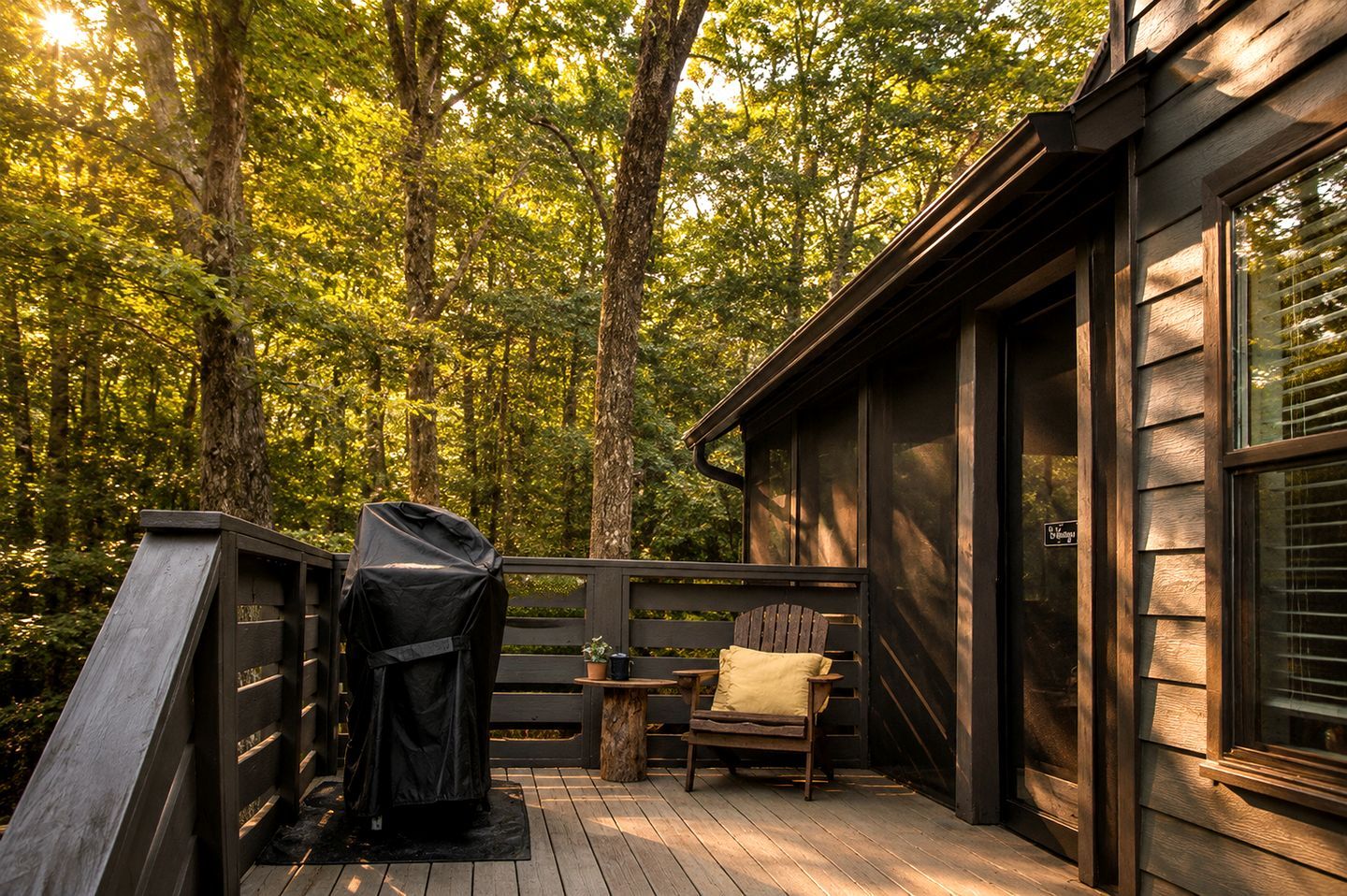 Una terraza de madera con una parrilla, una silla y una mesa, rodeada por un bosque.