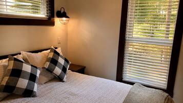 Un dormitorio con una cama, almohadillas de cuadros, una lámpara de pared y un ventanal con persianas.