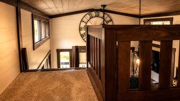 A wooden staircase with a carpeted landing, a large wall clock, and a hanging light fixture.