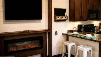 A modern kitchen with a flat-screen TV, a fireplace, wooden cabinets, a microwave, and a coffee maker.