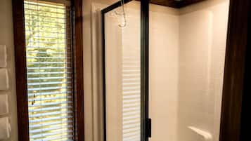 Een douche met glazen deur, houten balken en een raam met zonwering.