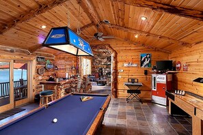 Une table de billard dans un chalet en bois, avec un coin bar, un téléviseur et un réfrigérateur Coca-Cola.