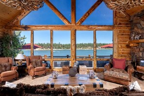 A log cabin interior with a large window overlooking a lake, furnished with leather sofas and a coffee table. - Outstanding Lake Cabin with Hot-Tub, Views and Game Room in California (Big Bear Lake)