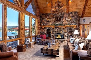 A log cabin interior with a stone fireplace, large windows overlooking a body of water, and rustic furnishings. - Outstanding Lake Cabin with Hot-Tub, Views and Game Room in California (Big Bear Lake)