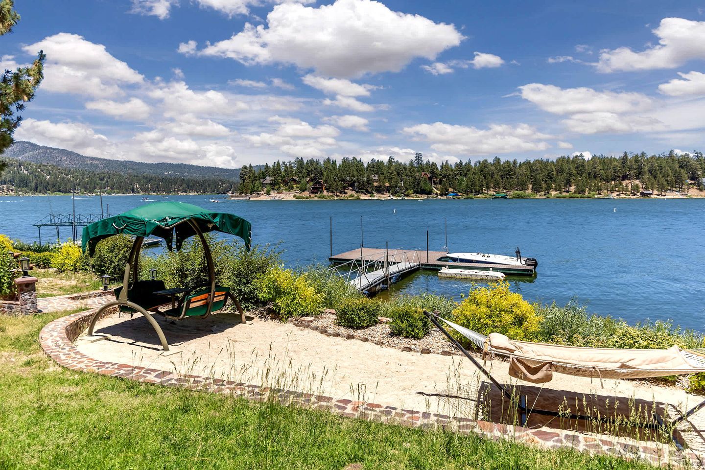 Un patio junto al lago con una silla mecedora, una zona de estar cubierta y un muelle.