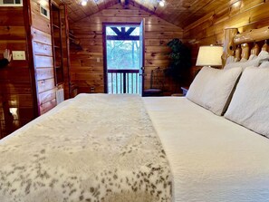 Ein Schlafzimmer einer Holzhütte mit einem großen Bett, einer Holztür und Blick durch die Tür.