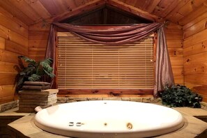 L’intérieur d’un chalet en bois, avec un jacuzzi, des murs en bois, une fenêtre avec des stores et une plante.