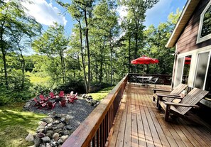 A wooden deck with outdoor seating, surrounded by trees and a stone fire pit. - Group Lake Cabin with Ping Pong Table Loaded with Kayaks in Wisconsin (Stone Lake)