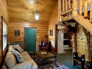 Ein Blockhaushaus-Interieur mit einer Couch, einem Sessel, einem Couchtisch, einer Holztreppe und einem Kamin.