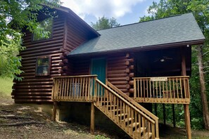 A log cabin with a wooden staircase leading to a porch, a green door, and a sign that reads 'HIDEAWAY CABIN.' - Group 4) The Hideaway (Eureka Springs)