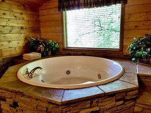 Ein Badezimmer mit einer Naturstein-Arbeitsplatte, einer weißen Badewanne und einem Fenster mit Jalousien.
