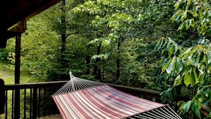 Een hangmat op een houten terras met uitzicht op een bos.