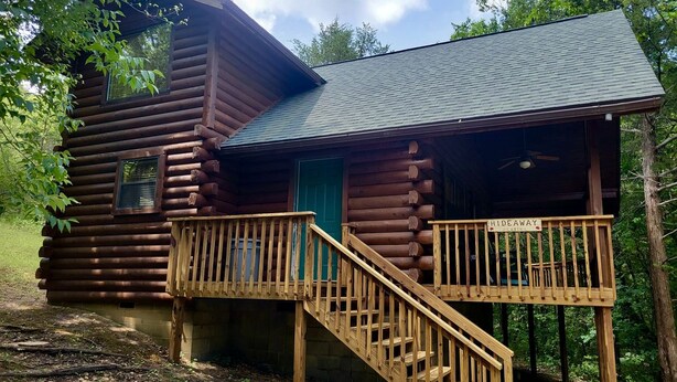 Een blokhut met een houten trap naar een veranda, een groene deur en een bordje met de tekst 'HIDEAWAY CABIN'.