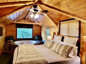 Ein Schlafzimmer in einer Blockhütte mit einem großen Bett, einer Badewanne und einem Deckenventilator.