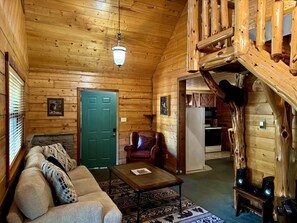 Ein Blockhaushaus-Interieur mit einer Couch, einem Sessel, einem Couchtisch, einer Holztreppe und einem Kamin.