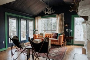 Un salon chaleureux avec un canapé, des fauteuils, un lustre et de grandes fenêtres.
