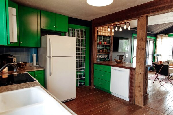 A kitchen with green cabinets, a white refrigerator, and a wooden dining area. - Family Glampsite: A Unique Cabin Retreat for Adventure in Tracy City, TN (Tracy City)
