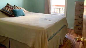 A bedroom with a bed, a dresser, a ceiling fan, and a window with curtains.