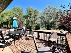 A wooden deck with outdoor furniture, including a table and chairs, and a blue umbrella. - Chic Cabin with Lake Views from the Deck in South Dakota (Hot Springs)
