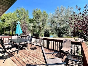 A wooden deck with outdoor furniture, including a table and chairs, and a blue umbrella. - Chic Cabin with Lake Views from the Deck in South Dakota (Hot Springs)