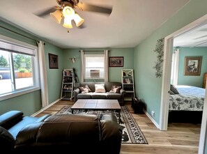 A room with a sofa, a coffee table, a bookshelf, a bed, and a window. - Chic Cabin with Lake Views from the Deck in South Dakota (Hot Springs)