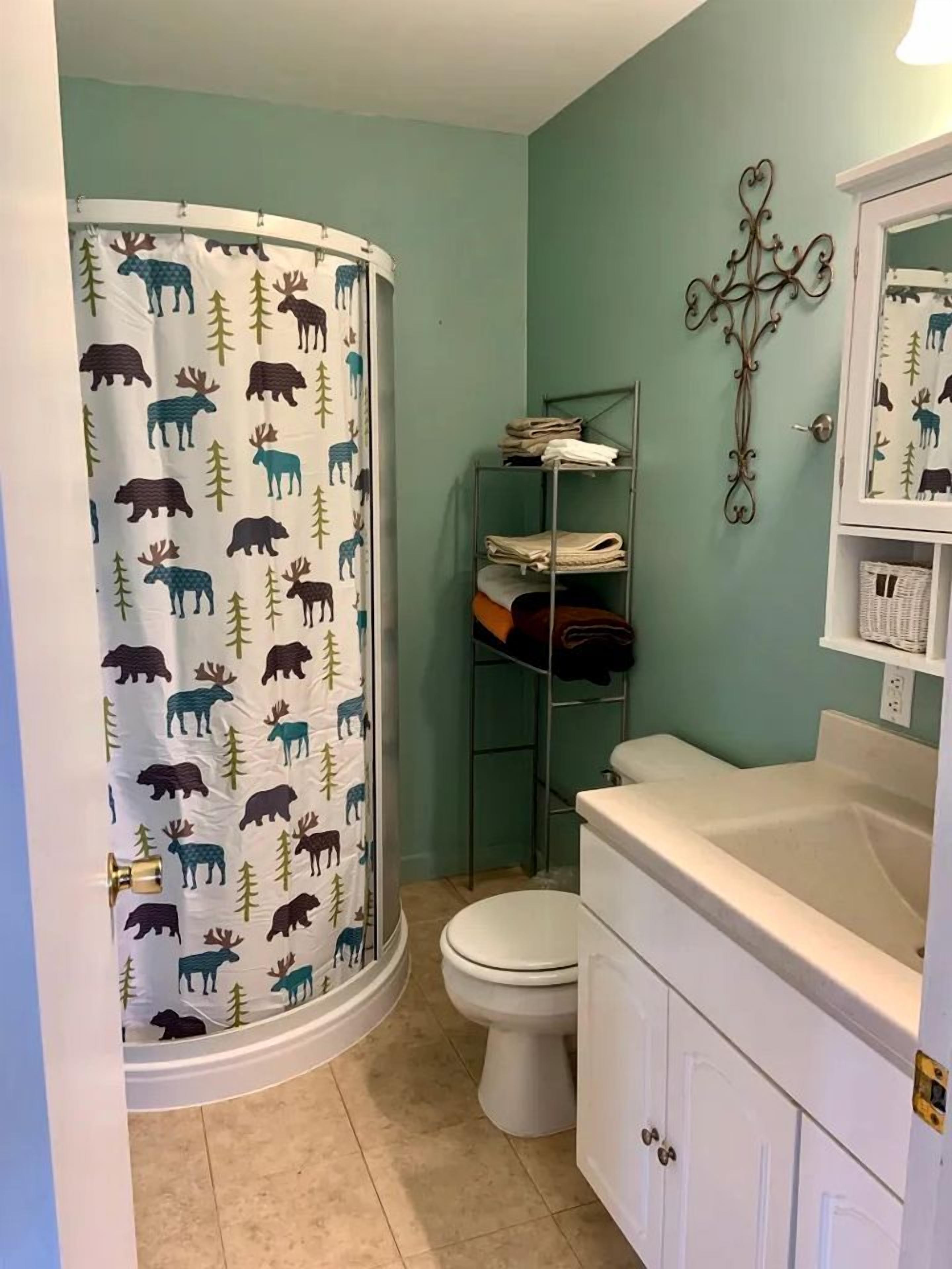 Un baño con cortina de ducha estampada con motivos animales, un inodoro, un estante de metal con toallas dobladas y un tocador blanco con espejo.