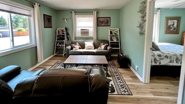 A room with a sofa, a coffee table, a bookshelf, a bed, and a window.