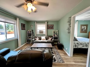 A room with a sofa, a coffee table, a bookshelf, a bed, and a window. - Chic Cabin with Lake Views from the Deck in South Dakota (Hot Springs)