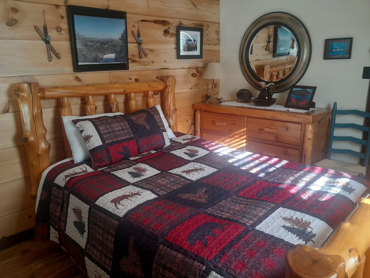Una cama de madera con colcha, un aparador, un espejo y cuadros en la pared.
