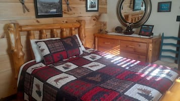 Una cama de madera con colcha, un aparador, un espejo y cuadros en la pared.