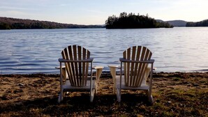 Kaksi Adirondack-tyylistä puutarhatuolia, jotka on sijoitettu niin, että ne osoittavat järvelle, jonka takana näkyy kaukainen saari ja metsäisiä kukkuloita.