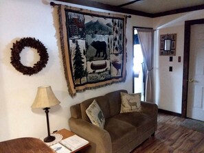 A living room with a couch, a lamp, a wall tapestry, and a door. - Pet-Friendly Ski Getaway near Gore Mountain Ski Resort in New York (Indian Lake)